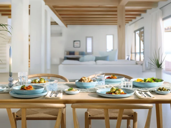 Un tavolo da pranzo in legno per quattro persone con piatti blu madreperla Aqua in una zona giorno luminosa e moderna.