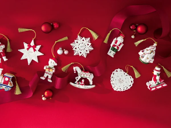 Assorted Christmas ornaments including a train, horse, nutcracker, snowflakes, and Santa on a red background with red ribbon and baubles.