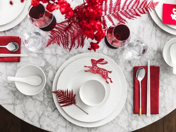 Manufacture von Villeroy & Boch ideal für Weihnachten Ein Manufacture Tischgedeck mit roten Akzenten, bestehend aus einem dekorativen Hasen und rotem Laub auf einer Marmoroberfläche.