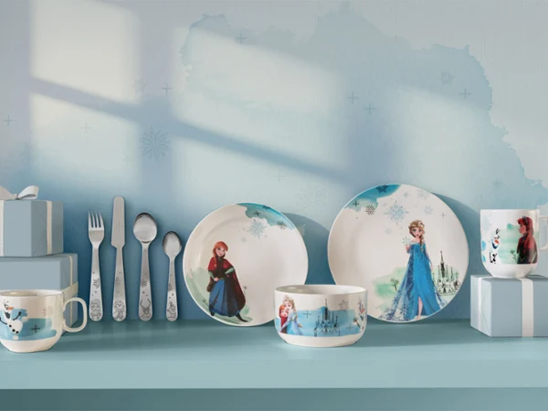 Kindergeschirr und -utensilien mit Frozen-Figuren, ausgestellt mit blauen Geschenkboxen auf einem blauen Regal.

