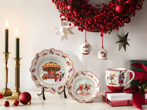 Świąteczna dekoracja bożonarodzeniowa z ozdobnymi talerzami, filiżankami i ozdobami z kolekcji Annual Christmas Edition Villeroy & Boch Świąteczna dekoracja bożonarodzeniowa z ozdobnymi talerzami z kolekcji Annual Christmas Edition marki Villeroy & Boch, filiżanką, świecami, zapakowanymi prezentami i wieńcem z czerwonych jagód z ozdobami i gwiazdkami.