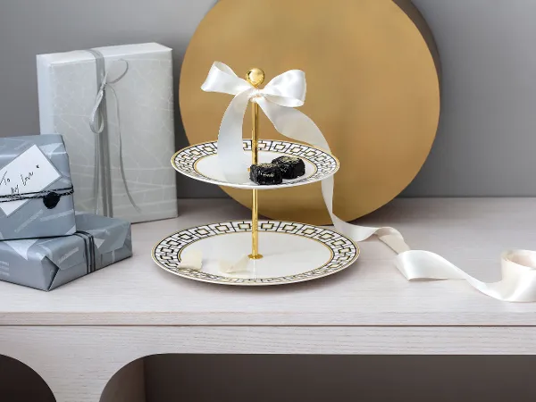 A MetroChic tiered cake stand with pastries surrounded by gift boxes A MetroChic tiered cake stand with pastries surrounded by gift boxes and a bow on a wooden table.