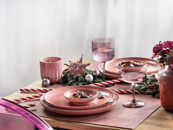 Festlicher Weihnachtstisch gedeckt mit rosa Perlemor Geschirr Ein festlich gedeckter Tisch mit rosa Perlemor Geschirr, dekoriert mit einem Schneeflockenornament, Zuckerstangen, rosa Blumen und silbernen Kugeln. Zwei Gläser, eine rosa Kerze und eine kleine Schüssel mit Essen sind ebenfalls vorhanden.