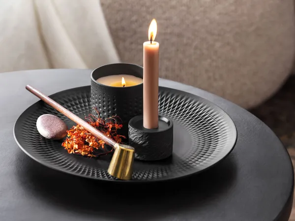 Decoratief zwart Manufacture bord met geurkaars Een brandende kaars met wierook en gedroogde bloemen op een decoratief zwart bord van Manufacture.
