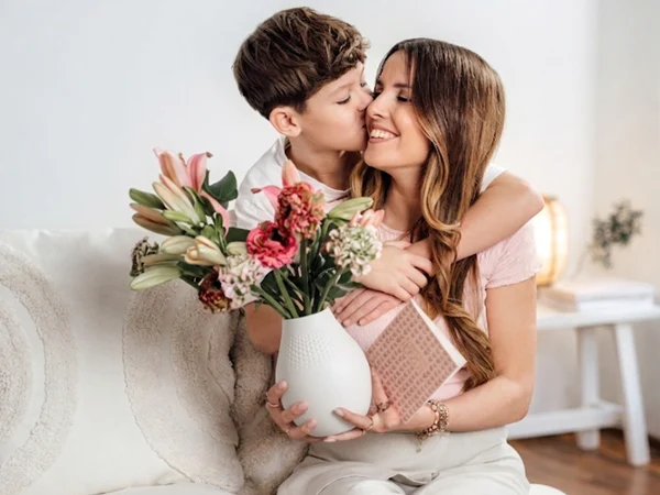 Mother holding Manufacture Collier White Vase Mother holding a Manufacture Collier white porcelain vase, showcasing modern textured design with a colorful floral arrangement.