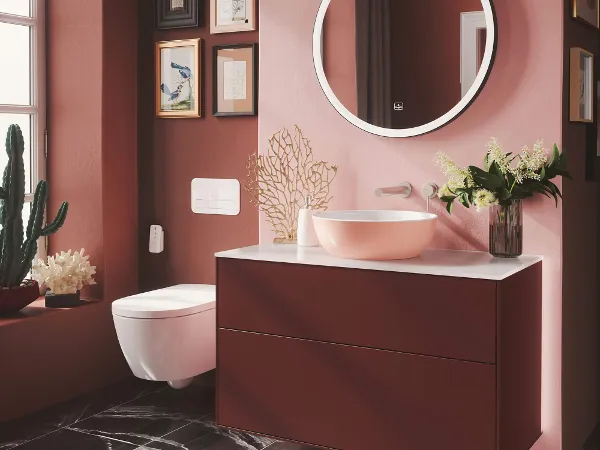 Pink Artis washbasin on a red Finion vanity unit Modern bathroom with a round mirror, a red Finion washstand and a pink Artis surface-mounted washbasin, with a dark pink wall and framed pictures