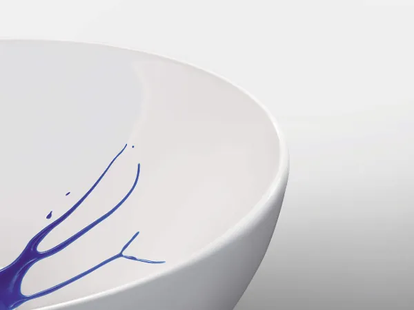 Biała umywalka z CeramicPlus Biała umywalka, z której krawędzi wąskimi strumieniami spływa niebieski płyn