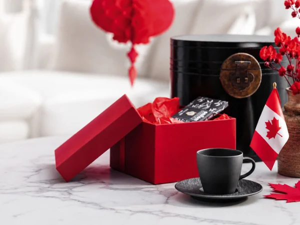 Manufacture rock espresso cup and saucer with red box with Canada flag Red gift box with tissue paper, black coffee cup and saucer, and a small Canadian flag displayed on a marble countertop, creating a festive Canada Day gift and coffee scene.
