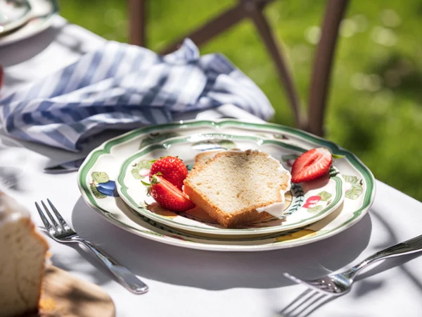 French Garden outdoor place setting A slice of pound cake and sliced strawberries on a decorative plate set on an outdoor table with utensils and a striped napkin.