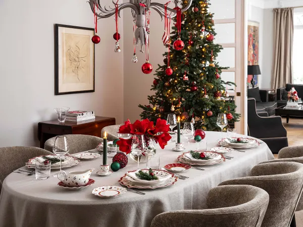 Toy's Delight crockery in a festively decorated dining room Festively decorated dining room with a table set for eight people. The table is set with festive crockery, candles and red flowers. Next to it is a Christmas tree with ornaments.