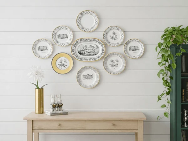 audun plates on a wall as art Wooden console table with gold vase and white flower, set against a white wall. Decorative plates arranged above, with bookshelf and trailing plant on the right.