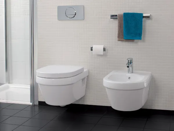 White Villeroy & Boch Architectura toilet and bidet Modern Architectura bathroom with a wall-mounted toilet, a bidet, a toilet roll holder and a towel holder with a blue-brown towel. The floor is covered with black tiles and there are small square white tiles on the wall.