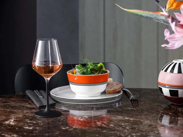 Memphis by Villeroy & Boch ideal for starters A dining room with a Memphis salad bowl, a wine glass, striped Memphis plates, a tropical flower in a Memphis vase and a marble table top.