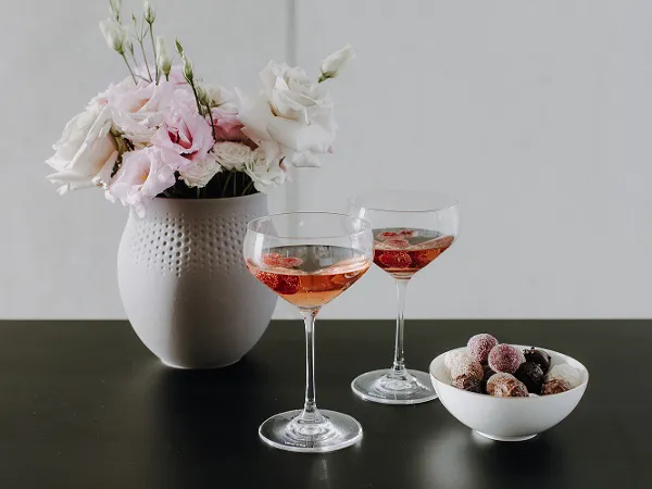 Purismo glasses, Manufacture bowl and Manufacture vase Two glasses of rosé wine, a white vase with flowers and a bowl of chocolates on a dark table.