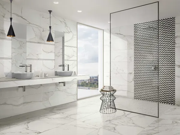 Modernes Badezimmer mit Artis Doppelwaschbecken von Villeroy & Boch Modernes Badezimmer mit weißen Marmoroberflächen, Artis Doppelwaschbecken von Villeroy & Boch, hängenden schwarzen Pendelleuchten, ebenerdiger Dusche mit geometrisch gemusterten Fliesen, Drahtkorbtisch und einem Fenster mit Blick auf die Stadt.