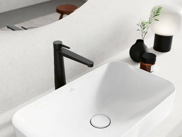 Schwarze Conum Waschbeckenarmatur mit Dekoration Ein modernes Waschbecken mit mattschwarzem Wasserhahn, minimalistischen Dekorationsgegenständen und einem gebogenen Aufsatzspiegel.