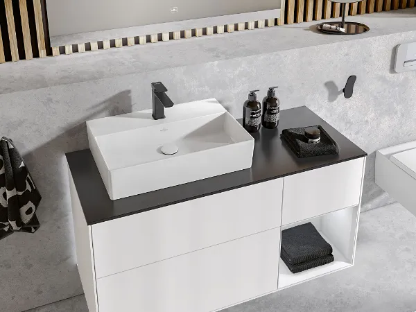 Un plan de toilette avec une vasque à poser Memento 2.0 blanche Un meuble minimaliste, noir et blanc, avec une vasque à poser rectangulaire blanche et une robinetterie chromée