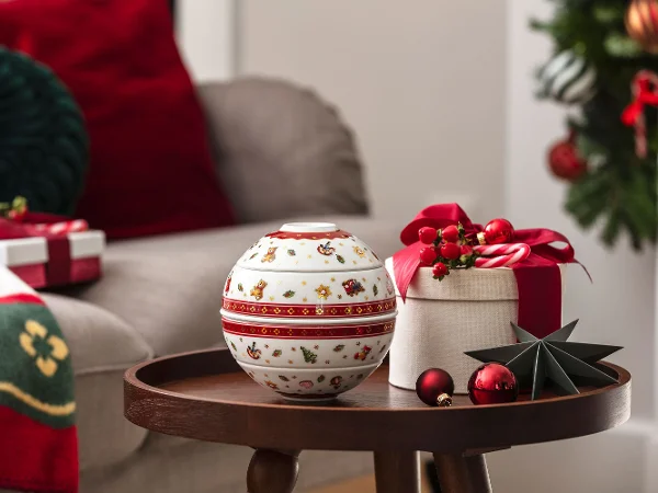 Spherical bowl set as decoration on a tray table A round tray table with a decorative spherical bowl set, a gift box, and baubles in a festive living room setting.