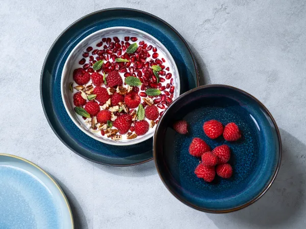 Two Crafted bowls, one with muesli and the other with raspberries Two Crafted bowls, one containing yoghurt with raspberries, pomegranate seeds and nuts, the other containing fresh raspberries.