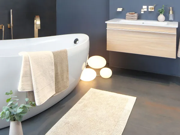 Villeroy & Boch Badewanne weiß mit Holz Badmöbeln Modernes Badezimmer mit freistehender weißer Badewanne, schwebendem Waschtisch, goldenen Armaturen, Handtüchern, Topfpflanze und beleuchteten Kugeln auf dem Boden