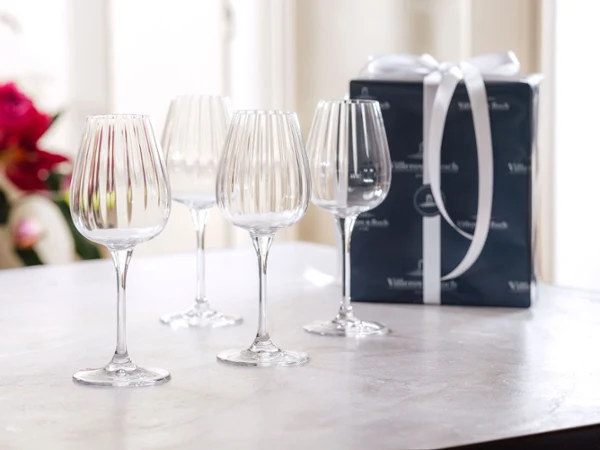 Four crystal wine glasses on a table next to a wrapped gift box with a white ribbon.