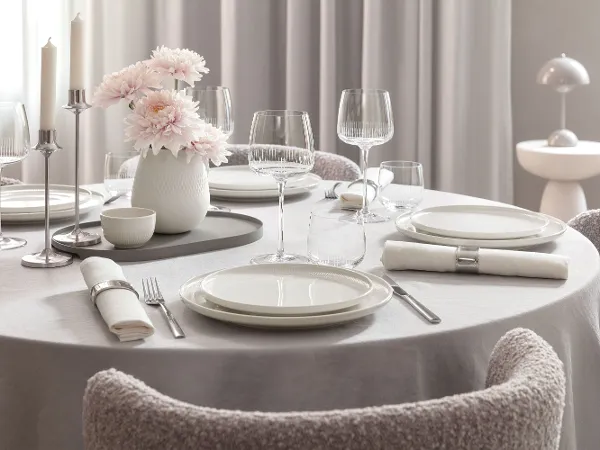 Ronde eettafel met witte Afina borden, Afina glazen, bestek, servetten en een vaas met roze bloemen.