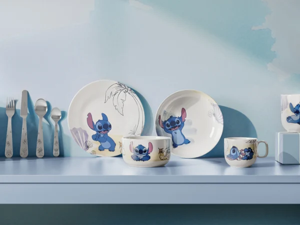 Eine Reihe von Tellern und Tassen der Kollektion Disney Stitch sind mit Cartoon-Motiven, die auf einem hellblauen Regal mit Utensilien ausgestellt.
