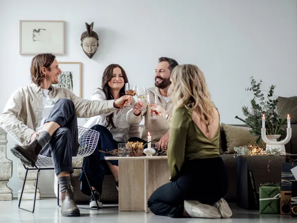Cosy toast with Winter Glow in the living room Four people toasting with Winter Glow glasses in a cosy living room decorated with Christmas accents.