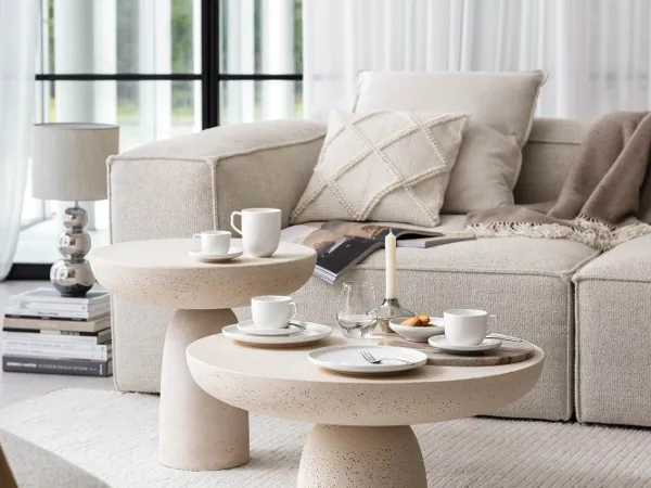 Weißes Afina Kaffee-Geschirr in modernem, hellem Wohnzimmer Ein gemütliches, modernes Wohnzimmer mit einem beigen Sofa, runden Couchtischen und darauf ein modernes Kaffee-Set mit Tassen und Tellern aus der Kollektion Afina von Villeroy & Boch.
