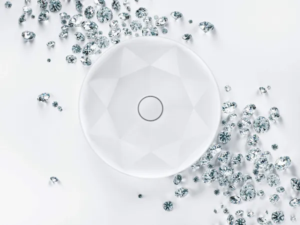 Octagon wastafel met diamanten van Villeroy & Boch Een ronde, witte wastafel met een geometrisch patroon wordt omringd door verspreide kleine en grote, heldere, facetgeslepen edelstenen op een witte achtergrond.