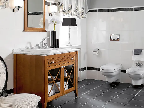 Cuarto de baño con lavabo de madera, inodoro, bidé y bañera de la colección Hommage Un cuarto de baño moderno con lavabo de madera, silla, inodoro y bidé de pared, bañera y toallero calefactor. El suelo es de baldosas negras, y las paredes blancas con detalles negros.