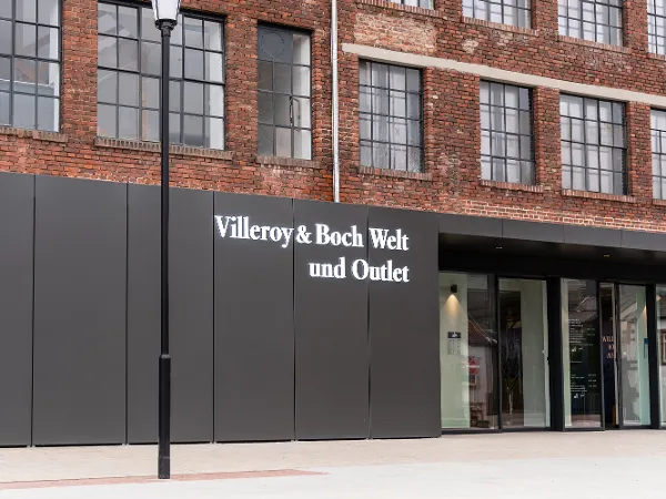 Eingangsbereich der Villeroy & Boch Welt und Outlet Schaufenster mit großen Fenstern und einem Schild mit der Aufschrift „Villeroy & Boch Welt und Outlet“ auf einem Backsteingebäude.