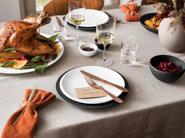 Manufacture flatware and dinnerware with NewMoon dinnerware and glassware on Thanksgiving table Thanksgiving dinner table with roast turkey, NewMoon wine glasses, Manufacture flatware and a plate with the phrase "Happy Thanksgiving".