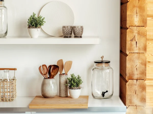 Rustic kitchen shelves with jars, potted herbs, wooden utensils Rustic kitchen shelves display jars, potted herbs, wooden utensils, cutting boards, and glasses beside a warm log wall, creating a cozy mood.