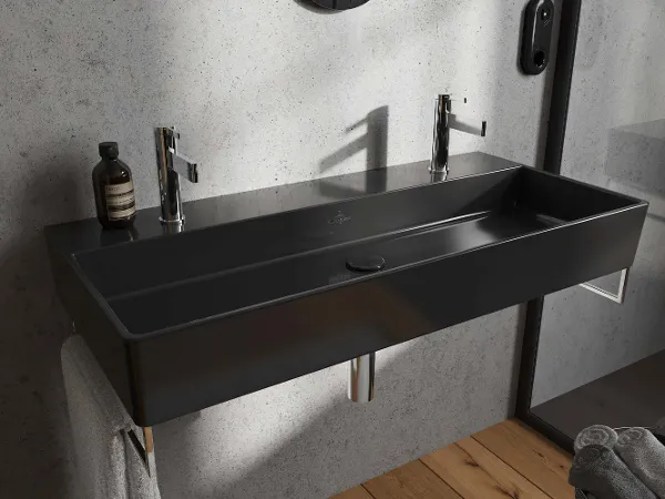 Doppelwaschbecken mit Chromarmaturen aus der Kollektion Memento Ein schwarzes Memento-Doppelwaschbecken mit Chromarmaturen und einer Flasche Seife. Der Raum hat eine graue Wand und auf der linken Seite hängt ein Handtuch.