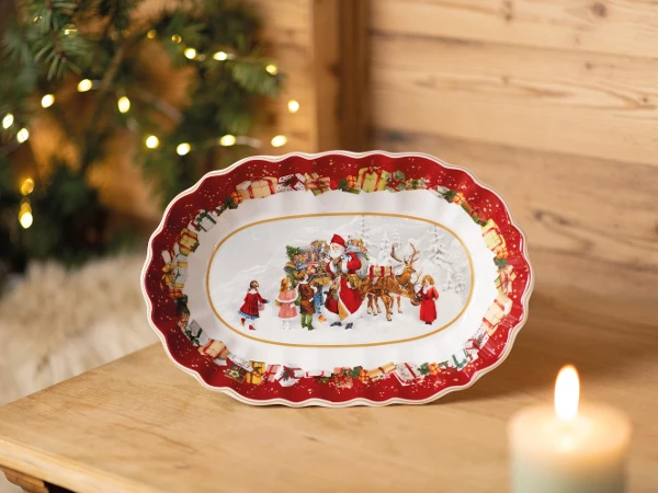 Festive ceramic plate with Santa, reindeer, and children in holiday outfits. Red border with gifts. Warm candlelight and fir branches in background. Cozy and joyful atmosphere.