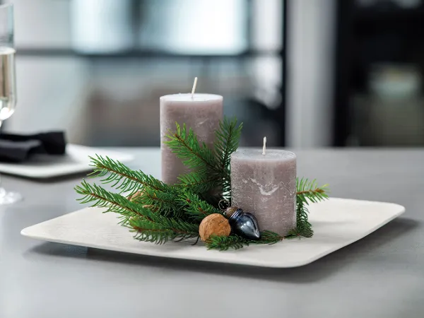 Manufacture Teller mit grauen Kerzen und weihnachtlicher Dekoration Zwei graue Kerzen, umgeben von Tannenzweigen und Nüssen, auf einem Manufacture Teller in weiß.