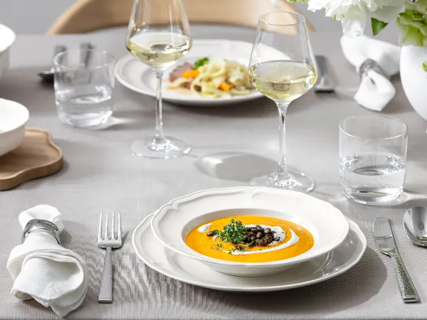 Manoir bowl with orange soup and a green garnish on top Close up shot of Manoir soup bowl on dinner table.