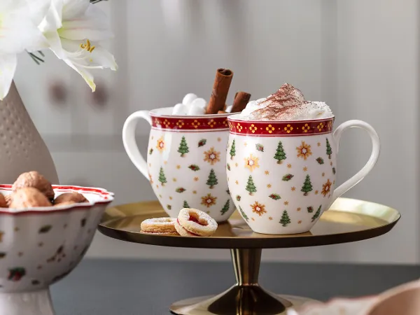 Two festive Toy's Delight cups Two festive Toy's Delight cups with whipped cream and cinnamon sticks on a tray, with biscuits and a flower vase next to them.