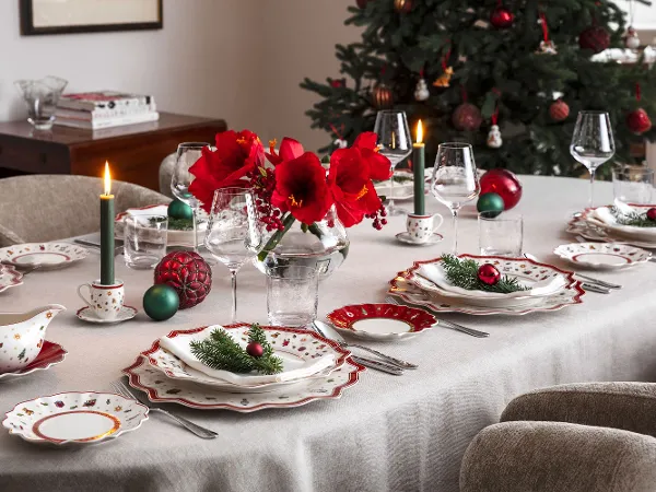 A festive dining table setting with elegant Toy's Delight crockery A festive dining table setting with elegant Toy's Delight crockery, lit candles, red flowers in a vase and Christmas decorations, with a decorated Christmas tree in the background.
