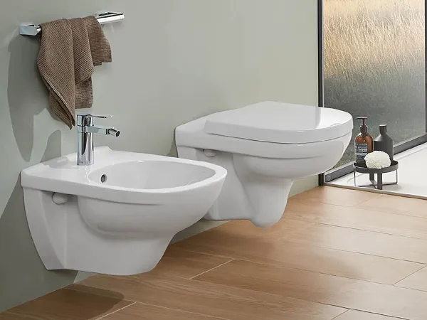 Modern bathroom with a toilet from the O.novo collection An O.novo wall-mounted toilet and bidet in a modern bathroom with a full-length window and view. Above it is a picture rail with abstract art.
