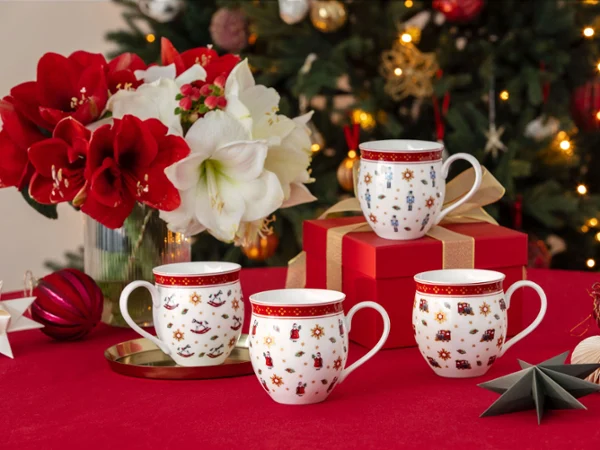 Four festive cups on a red tablecloth with flowers, ornaments, gifts, and a decorated Christmas tree in the background.