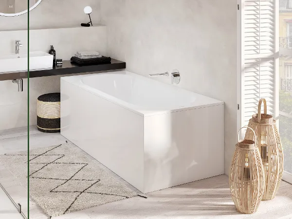 Oberon Vorwandbadewanne in edlem weiß Modernes Badezimmer mit weißer Oberon Badewanne, rundem Spiegel über dem Waschbecken, Teppich mit geometrischem Muster und natürlichem Licht durch ein großes Fenster. Neben der Wanne sind zwei korbartige Laternen angebracht.