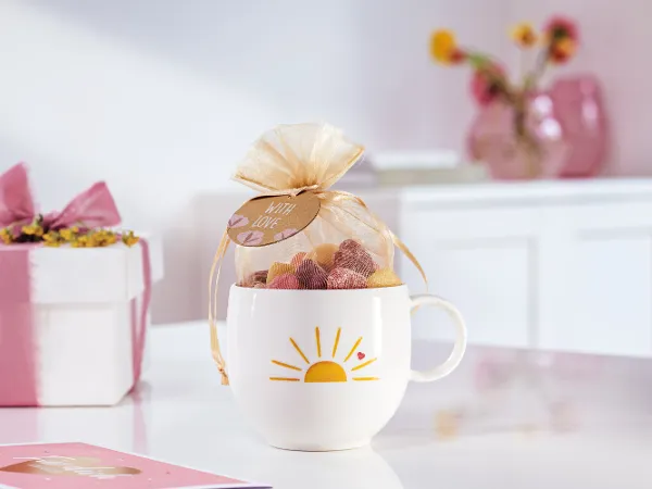 Tasse With Love mit Bonbons gefüllt With Love Tasse mit gelber Sonne und Herzchen-Motiv als Geschenk mit Süssigkeiten vorbereitet.