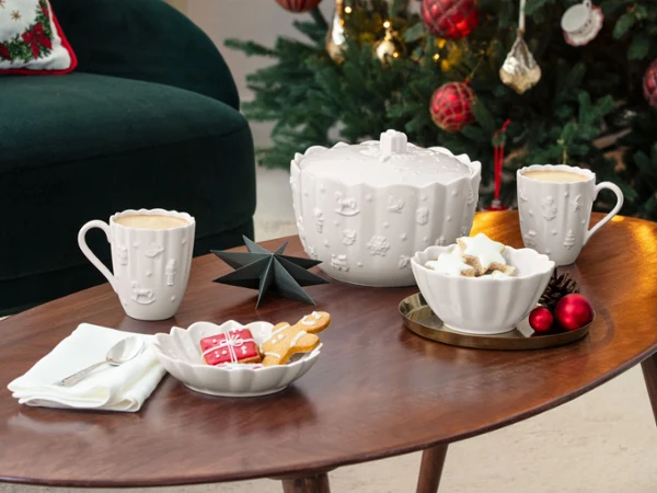 Toy’s Delight Royal Classic mugs A decorated Christmas tree with red ornaments stands behind a coffee table set with mugs, cookies, and festive decorations in a cozy living room.