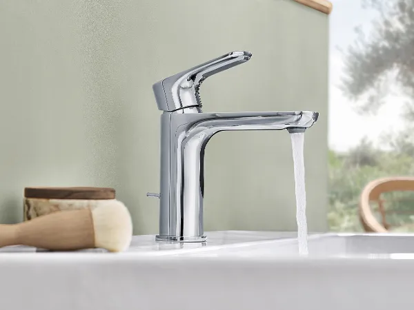 Modern chrome tap with running water A modern chrome tap with running water installed on a white O.novo washbasin. Next to it are a brush and a wooden container.