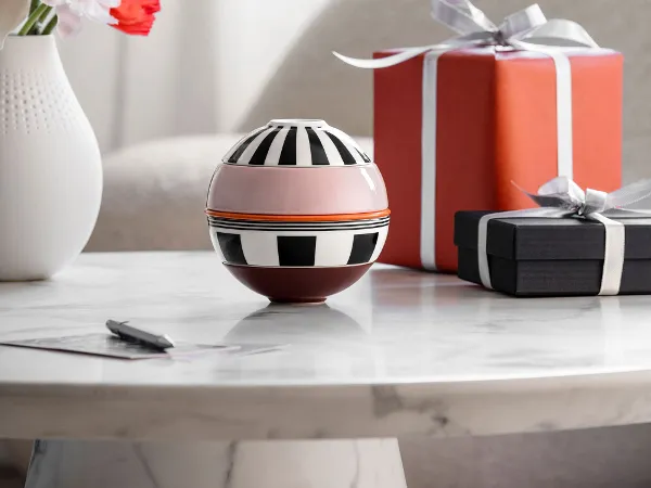 La petite Boule Memphis and two wrapped gifts stand on a table. La petite Boule Memphis from Villeroy & Boch and two wrapped gifts stand on a marble table, with a vase of flowers in the background.