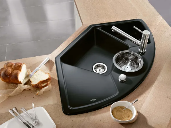 Black Solo Eck kitchen sink with bakery items Black Solo Eck corner sink in a kitchen with crockery and cutlery, next to it bakery items and a bowl of sugar on a wooden counter.