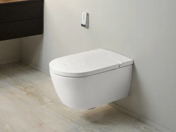Wall-mounted ViClean shower toilet with remote control Modern bathroom with a Villeroy & Boch wall-mounted ViClean toilet, grey tiles, a floating shelf with towels and decor and warm lighting.