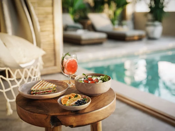 Poolside summer lunch with salad, grilled sandwich, fresh fruit, and a citrus cocktail served on natural stoneware tableware in a luxurious outdoor setting.